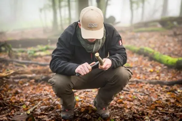 Mann bearbeitet Holzstück mit Messer im Laubwald