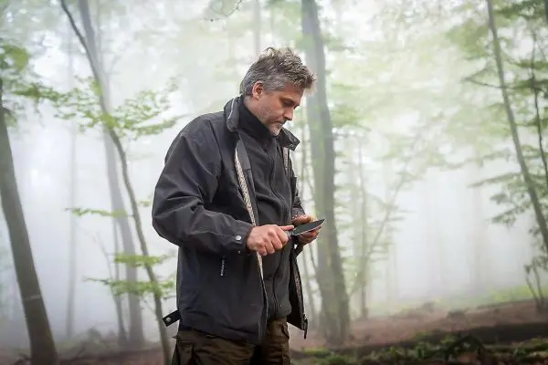 Mann hält ein Messer in der Hand und bearbeitet Holz im Wald