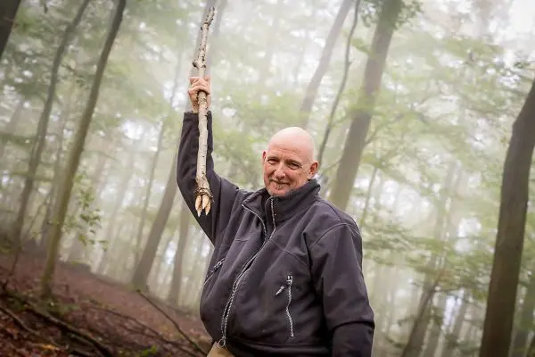 Mann hält einen Stock in einer bewaldeten Umgebung hoch