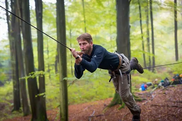 Mann überquert eine selbstgebaute Seilbrücke zwischen Bäumen