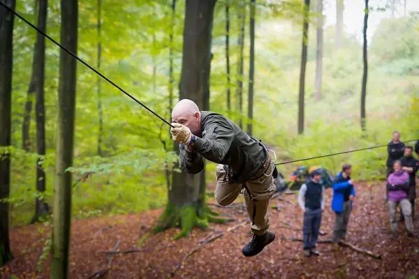 Mann überquert eine selbstgebaute Seilbrücke zwischen Bäumen