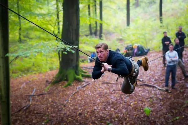Mann überquert eine selbstgebaute Seilbrücke zwischen Bäumen im Wald