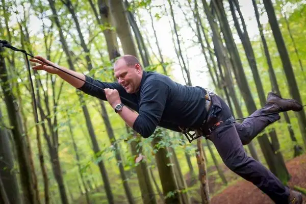 Mann überquert mit Seil eine Baumreihe im Wald