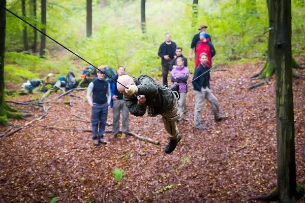 Mann überquert selbstgebaute Seilbrücke, während Gruppe zuschaut
