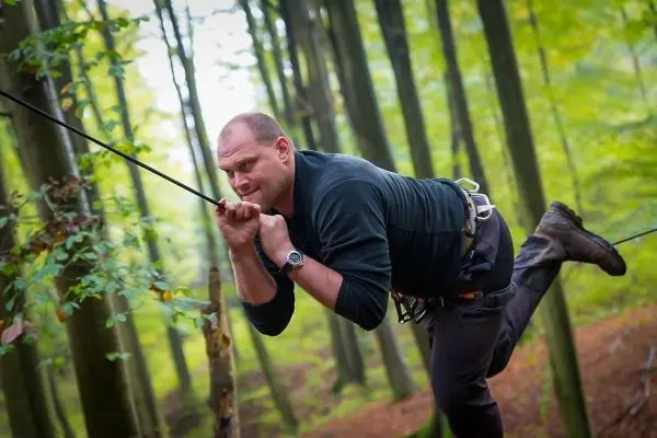 Mann überquert selbstgebaute Seilbrücke zwischen Bäumen im Wald