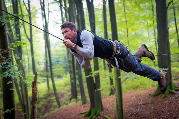 Mann überquert selbstgebaute Seilbrücke zwischen Bäumen im Wald
