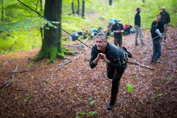 Mann überquert selbstgebaute Seilbrücke zwischen Bäumen im Wald