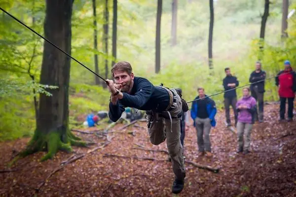 Mann überquert selbstgebaute Seilbrücke zwischen Bäumen im Wald