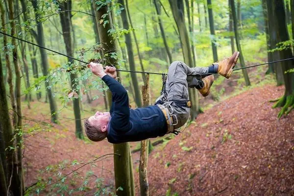 Mann überquert selbstgebaute Seilbrücke zwischen Bäumen im Wald