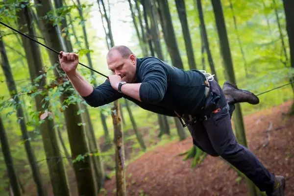 Mann überquert selbstgebaute Seilbrücke zwischen Bäumen im Wald