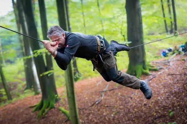 Mann überquert selbstgebaute Seilbrücke zwischen Bäumen im Wald
