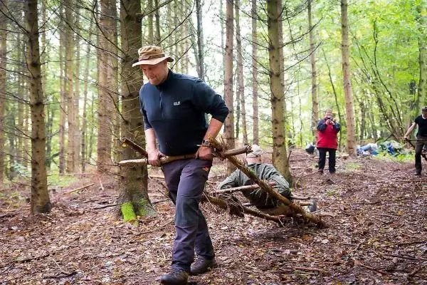 Mann zieht improvisierte Trage aus Ästen durch den Wald