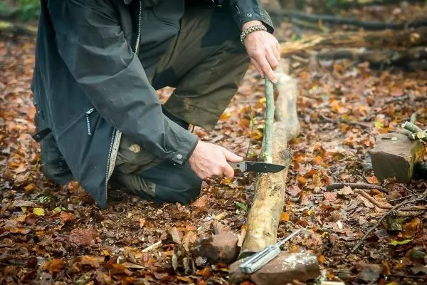 Messer bearbeitet einen Holzstock auf dem Boden im Laub