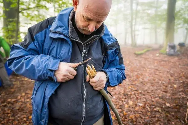 Messer bearbeitet Holzstück zur Herstellung eines Werkzeugs im Wald