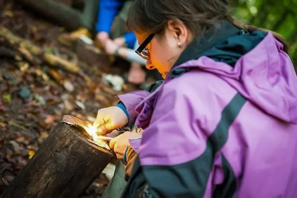 Person entzündet Feuer mit einem Feuerstein auf einem Baumstamm beim Survival Training