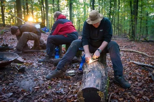 Person schnitzt an einem Baumstamm im Wald beim Survival Training