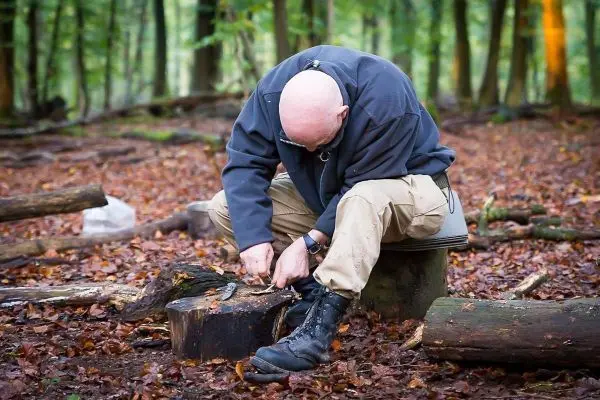 Person schnitzt mit einem Messer auf einem Baumstumpf im Wald