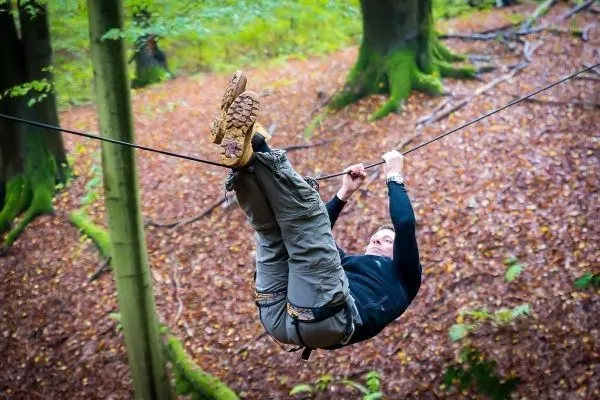 Person schwingt an selbstgebauter Seilbrücke durch den Wald