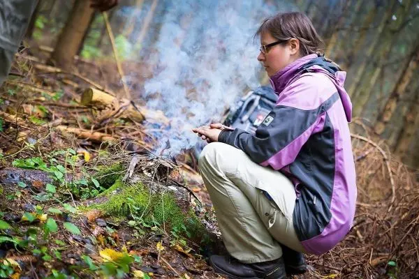 Person sitzt neben rauchendem Feuer im Wald