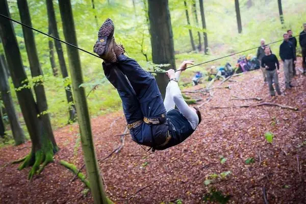Person überquert selbstgebaute Seilbrücke zwischen Bäumen im Wald