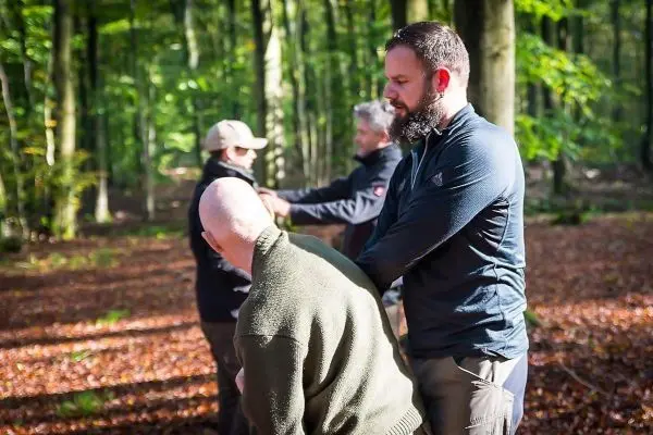 Person zeigt einer anderen Person eine Technik im Wald
