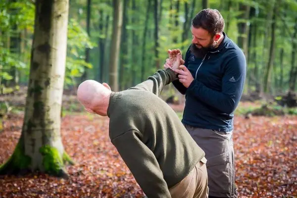 Person zeigt einer anderen Person eine Technik im Wald