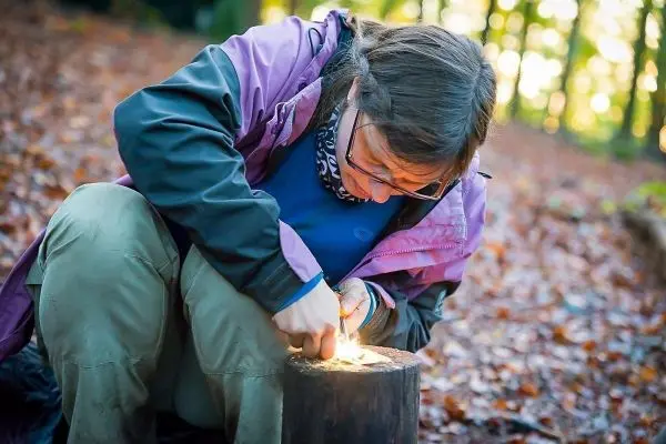 Person zündet Feuer auf einem Holzstück im Wald