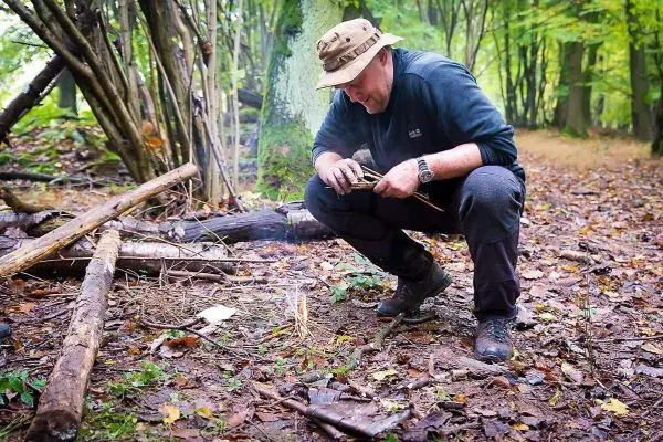 Person zündet Feuer mit Holzstücken im Wald beim Survival Training