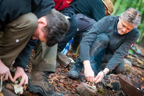 Person zündet Feuerstelle im Wald an beim Survival Training