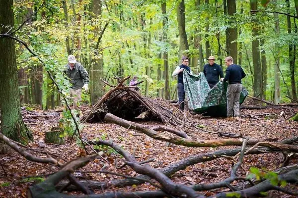 Tarp-Notunterkunft wird von mehreren Personen im Wald aufgebaut