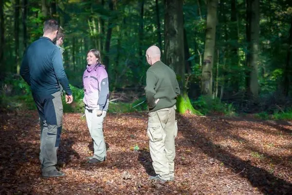 Vier Personen stehen im Wald auf Laub und unterhalten sich