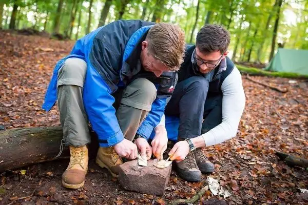 Zwei Personen bearbeiten Zunder auf einem Stein im Wald