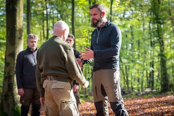 Zwei Personen stehen sich gegenüber und führen eine praktische Übung im Wald durch