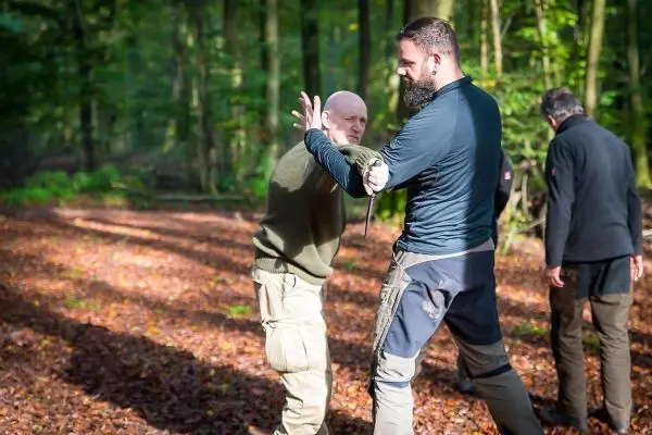Zwei Personen üben eine Selbstverteidigungstechnik im Wald auf Laub