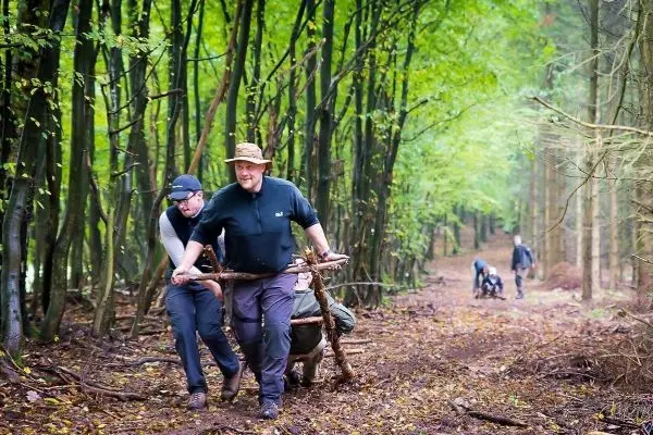 Zwei Personen ziehen eine Holzschubkarre auf einem Waldweg