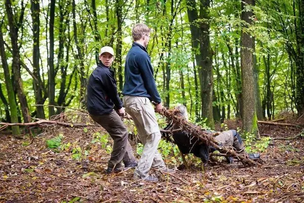 Zwei Personen ziehen eine improvisierte Trage aus Ästen durch den Wald