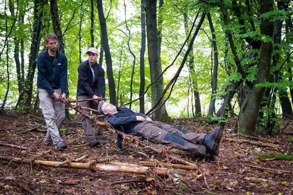 Zwei Personen ziehen eine improvisierte Trage aus Ästen mit einer liegenden Person