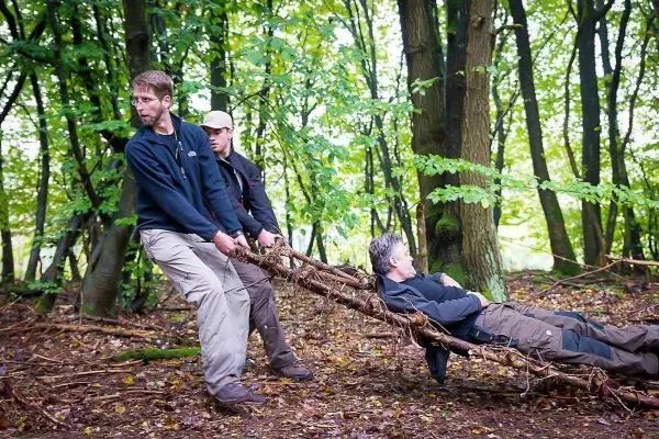 Zwei Personen ziehen eine improvisierte Trage durch den Wald