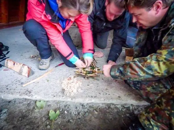 Drei Personen bereiten ein Zundernest aus kleinen Ästen und Rinde vor