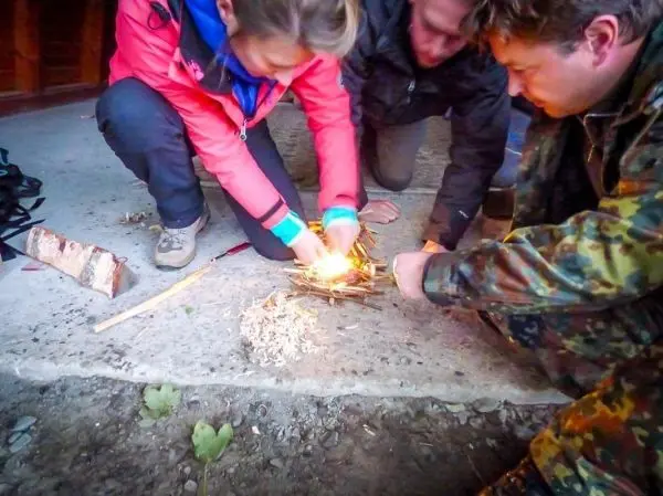 Feuerstahl erzeugt Funken auf Zunder während mehrere Personen um das Feuer herum arbeiten