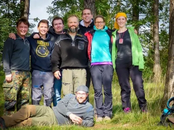 Gruppierung von neun Personen im Freien, umgeben von Bäumen und Gras