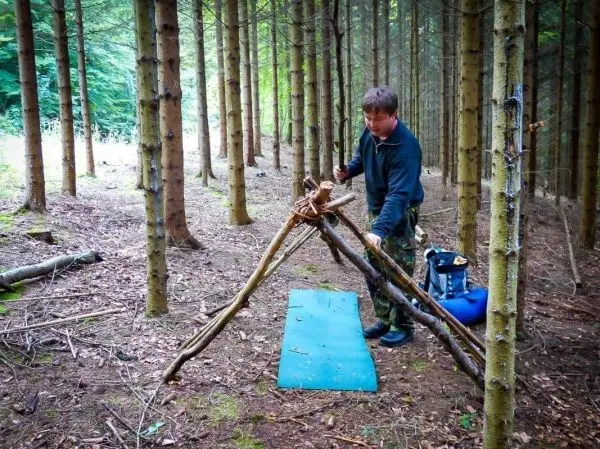 Mann baut eine selbstgebaute Konstruktion aus Ästen im Wald