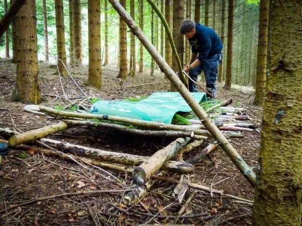 Mann baut eine Tarp-Notunterkunft aus Ästen im Wald