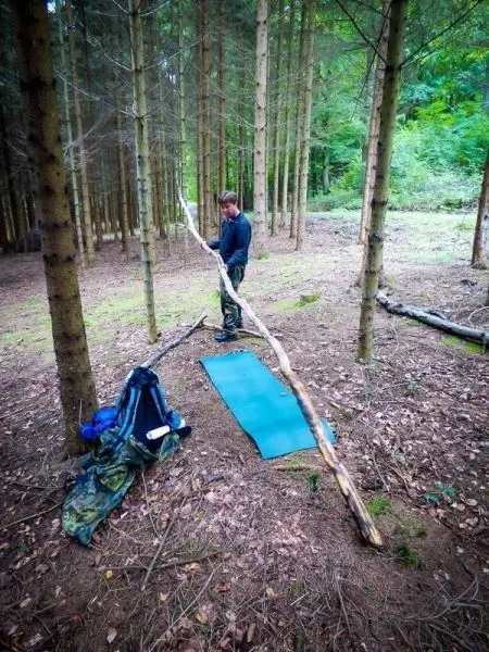Mann steht neben einer blauen Matte und hält einen langen Stock in einem Wald