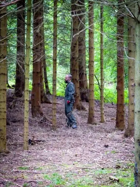 Mann steht zwischen Bäumen im Wald und betrachtet die Umgebung