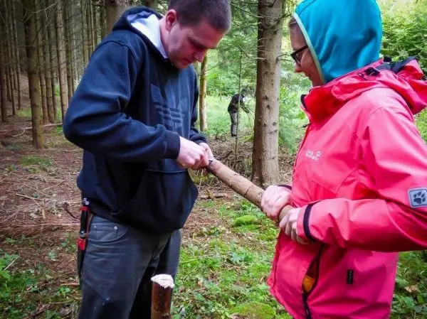 Messer bearbeitet Holzstück, während zwei Personen zusammenarbeiten