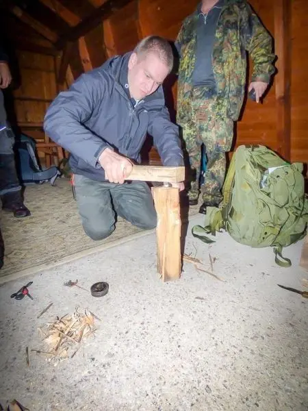 Person bearbeitet Holzstück mit einem Werkzeug beim Überlebenstraining