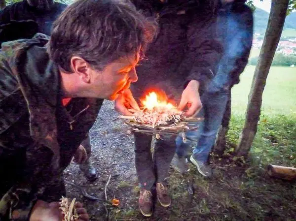 Person bläst auf ein Feuer aus Zunder und Ästen beim Survival Training