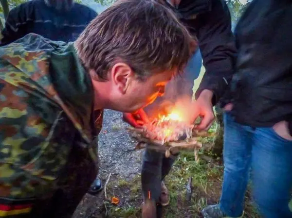 Person bläst auf ein Feuer aus Zweigen und Papier