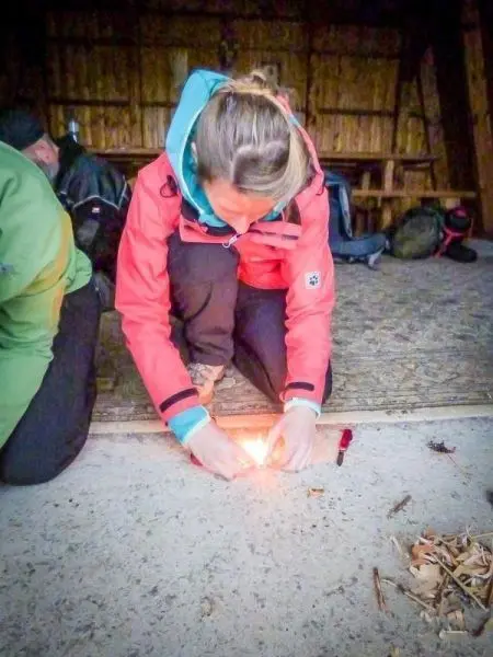 Person entzündet Feuer mit einem Feuerzeug auf dem Boden beim Survival Training